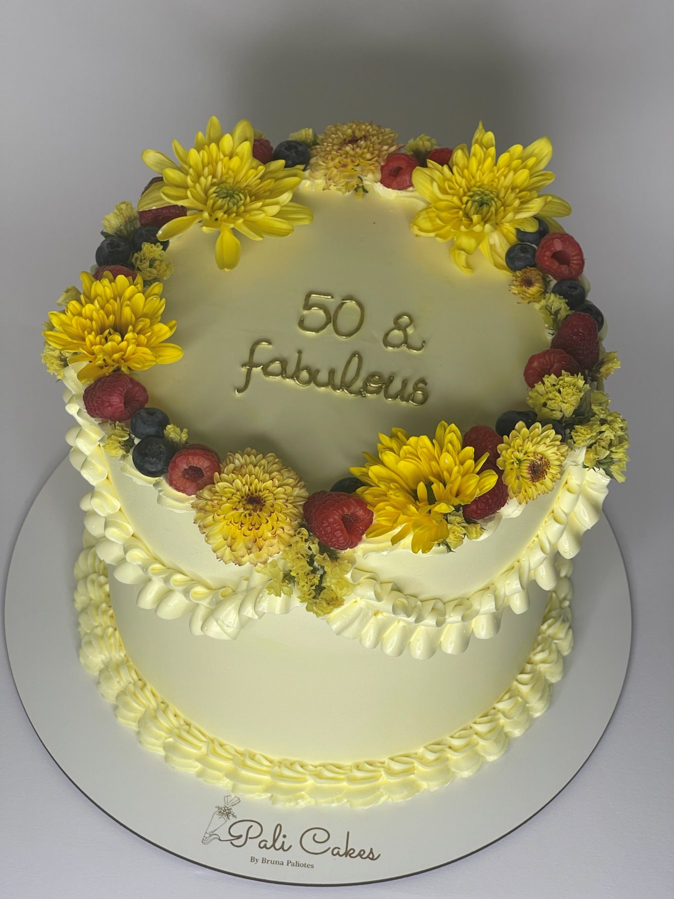 Bolo branco decorado com flores amarelas e frutos vermelhos frescos produzido pela Pali Cakes