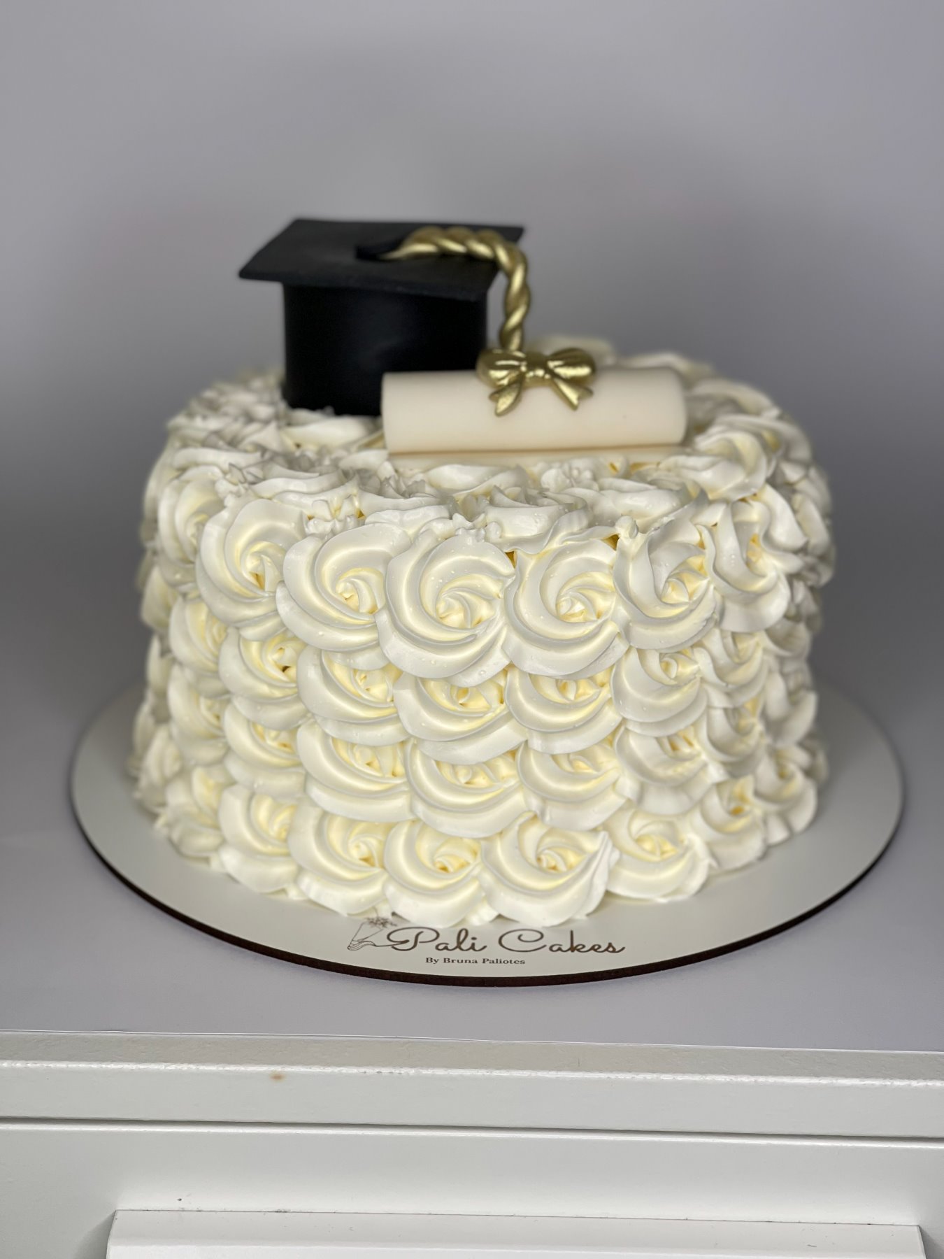 Bolo branco texturado com rosetas de chantilly e topo de finalista produzido pela Pali Cakes