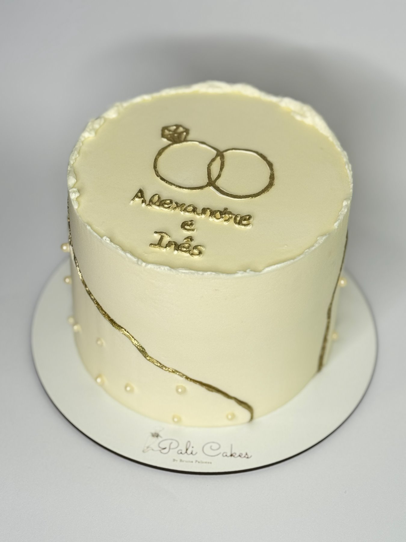 Bolo elegante com desenho de alianças douradas e pérolas produzido pela Pali Cakes