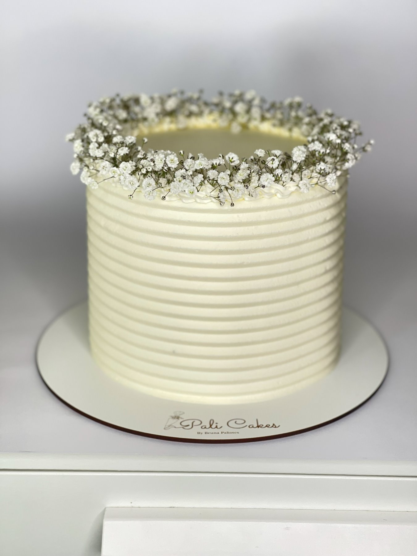 Bolo branco texturado com coroa de flores naturais produzido pela Pali Cakes