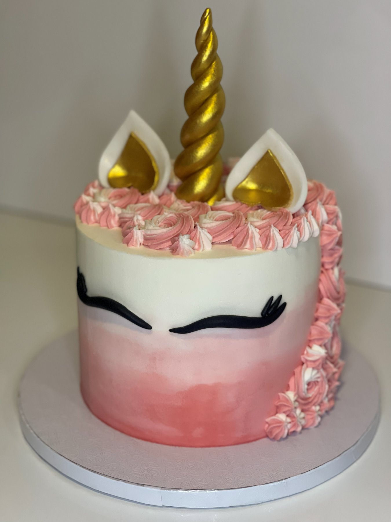Bolo temático de unicórnio com corno dourado e rosetas cor-de-rosa produzido pela Pali Cakes